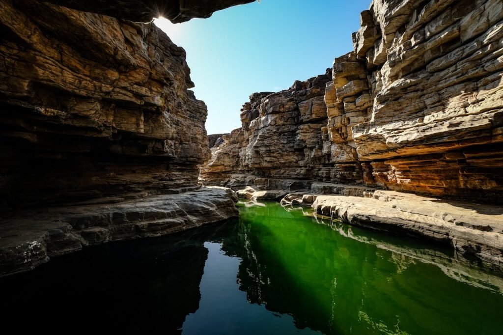 A stunning canyon scene with a calm river reflecting the rocky landscape under a blue sky.
